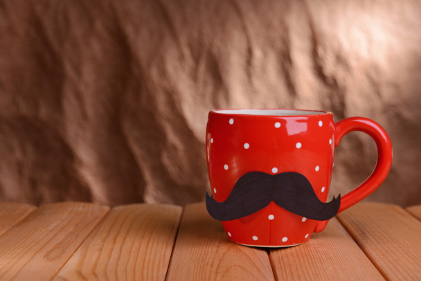 Cup with mustache on table on brown background - Fotoğraf, Görsel