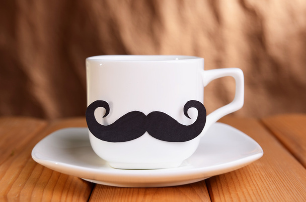 Cup with mustache on table on brown background - Foto, Bild