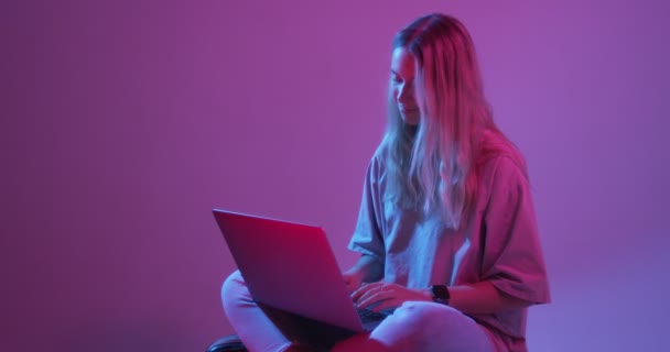 4k video of modern young girl blogger with laptop, typing on computer. Colored Neon light and background - Video, Çekim
