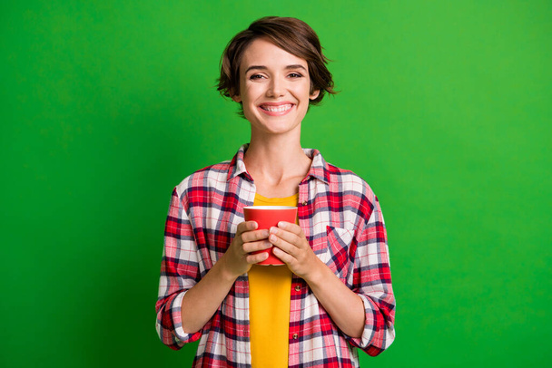 Photo of optimistic nice short hairstyle lady hold cup wear yellow checkered shirt isolated over vivid green color background - Фото, изображение
