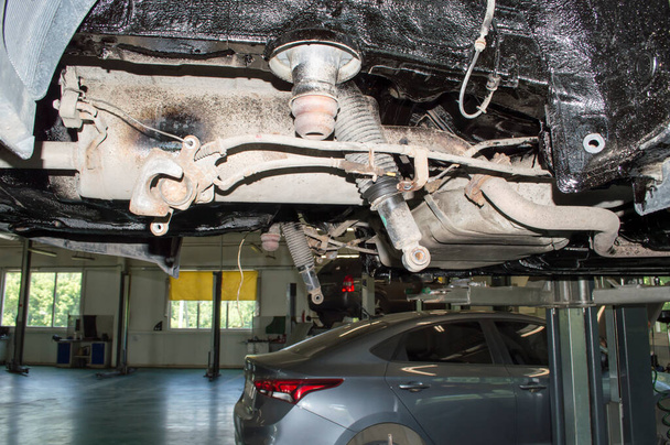 View of the rear suspension of the car with the rear beam removed. The car is hanging on a lift in an auto repair shop. - Photo, Image