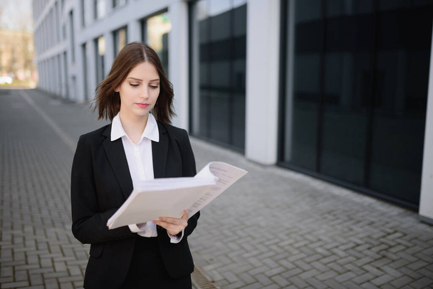 A confident business woman stands with documents near the business center. - Φωτογραφία, εικόνα