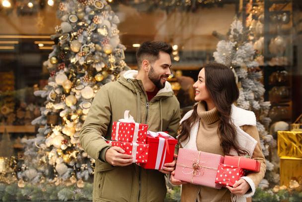 Casal encantador com presentes perto da loja decorada para o Natal ao ar livre - Foto, Imagem