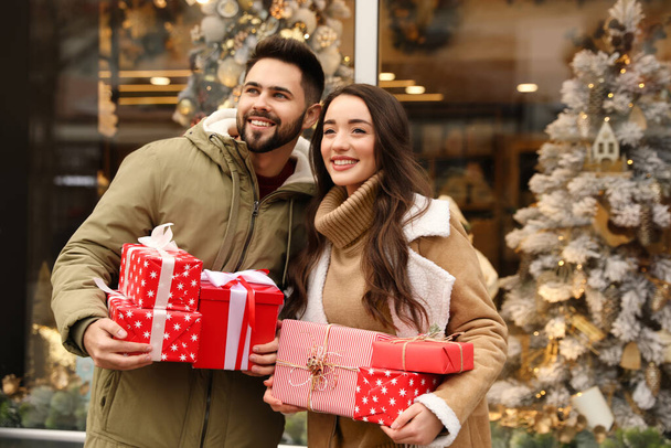 Lovely couple with presents near store decorated for Christmas outdoors - Foto, immagini