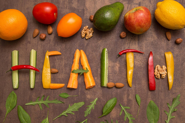 Word Health written with letters from different vegetables, fruits, nuts and greens on rustic wooden background. Organic ingredients for raw healthy diet - Foto, Bild