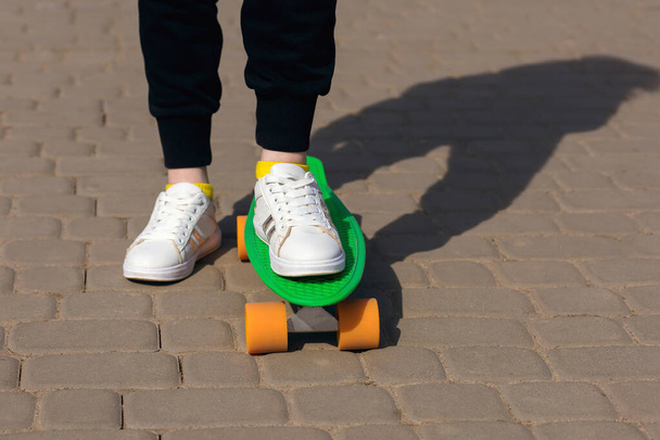 Een kind rijdt op een groen skateboard of penny board in het park. De gezondheidsvoordelen van buitensporten. Close-up van het skateboard en de benen - Foto, afbeelding