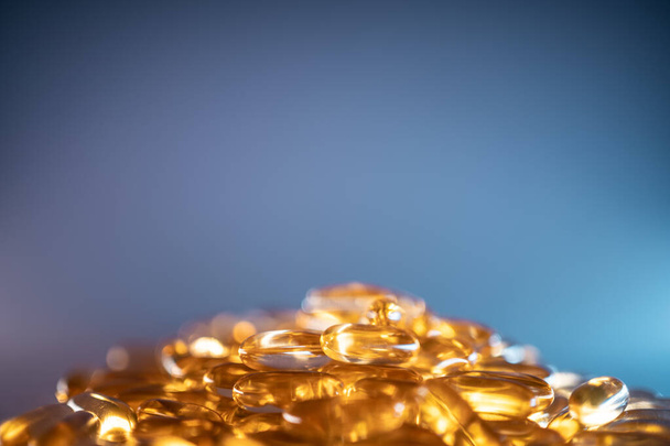 handful of golden fish oil capsules omega 3 vitamins on blue background - Фото, изображение