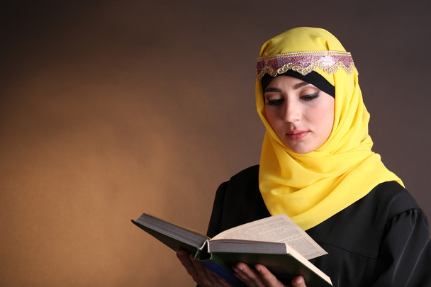 Beautiful muslim arabic woman reading book on dark color background - Φωτογραφία, εικόνα