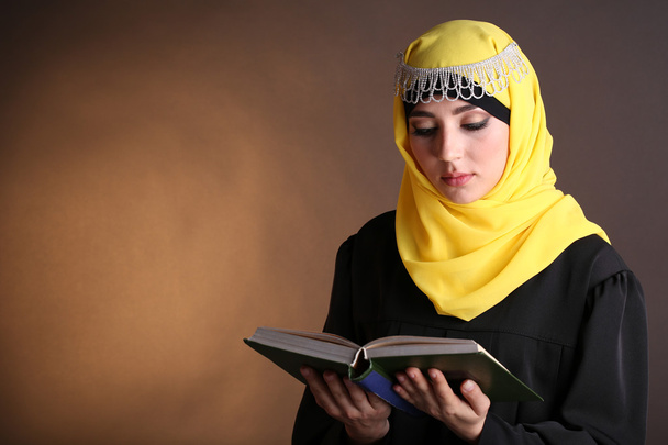Beautiful muslim arabic woman reading book on dark color background - 写真・画像