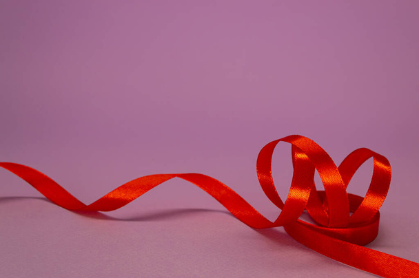 Red satin ribbon curls on a lilac background, free space. - Foto, afbeelding