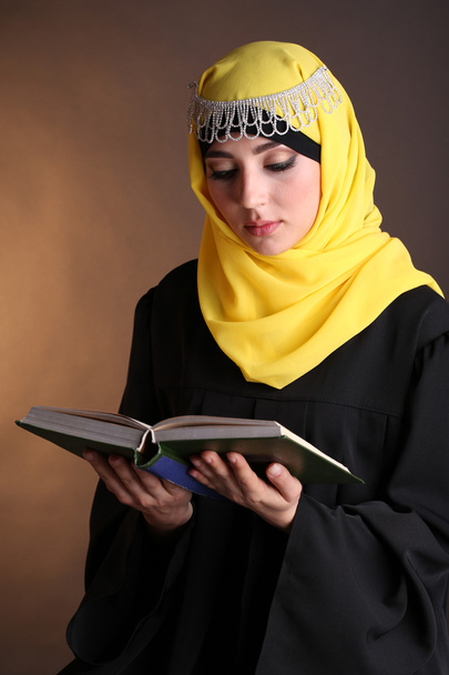 Beautiful muslim arabic woman reading book on dark color background - Φωτογραφία, εικόνα