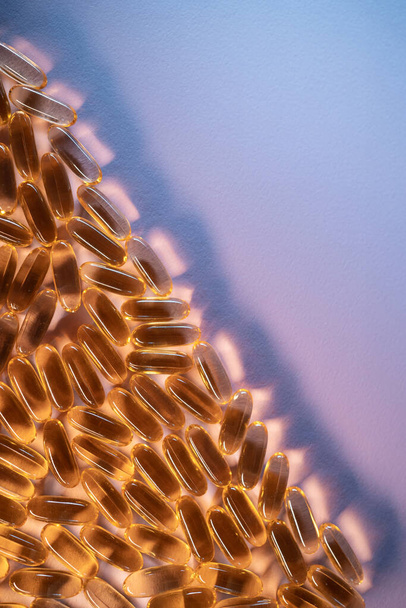 handful of golden fish oil capsules omega 3 vitamins on purple background - Zdjęcie, obraz