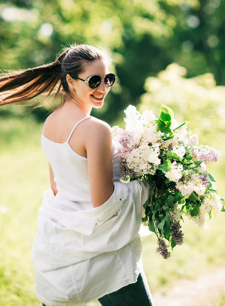 Happy smiling pretty woman in glasses with a large bouquet of wildflowers walking in a summer meadow - Foto, afbeelding