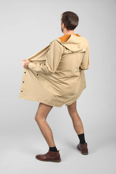 Exhibitionist exposing naked body under coat on light background, back view - Foto, afbeelding