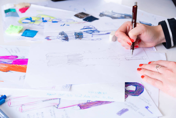 mladá bruneta žena navrhuje módní šaty kresba s barevnými tužkami. Různé barevné módní kresby a náčrtky - Fotografie, Obrázek