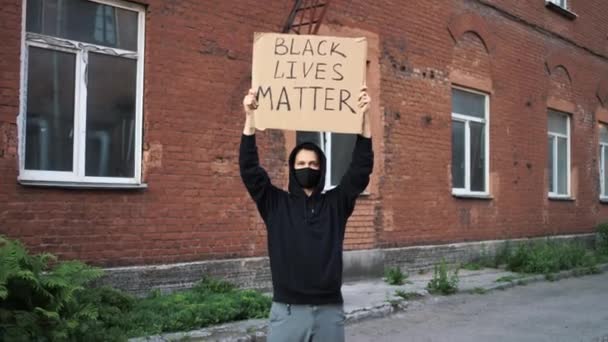 Hombre con máscara se para con póster de cartón en las manos - BLACK LIVES MATTER - Metraje, vídeo