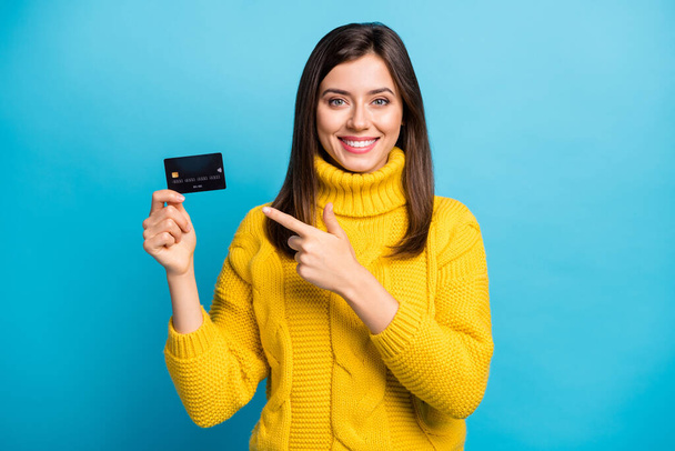 Photo of sweet shiny young lady wear yellow sweater pointing finger credit card isolated blue color background - Fotoğraf, Görsel