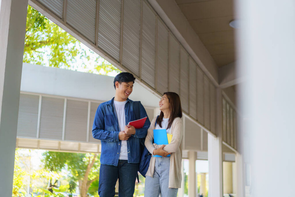 Két ázsiai pár egyetemista sétál és beszél az osztályhoz a sétányon egy gyönyörű napos napon az egyetemen. - Fotó, kép