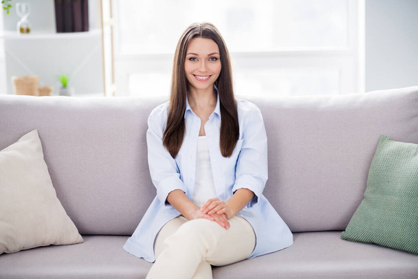 Photo of nice optimistic brunette long hairdo lady sit on coach wear blue shirt trousers alone at home - Zdjęcie, obraz