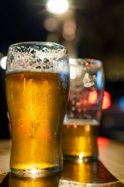 δύο ποτήρια χρυσαφένια μπύρα, ένα από τα οποία είναι σχεδόν έτοιμο. - Φωτογραφία, εικόνα