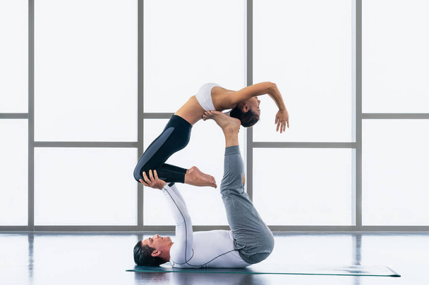 diverse athletic couple caucasian and asian in sportswear practicing acro yoga or yoga partner together in gym and fitness club. Athletic couple healthy and wellness lifestyle. - 写真・画像