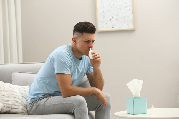 Ill man using nasal spray on sofa at home - Fotoğraf, Görsel