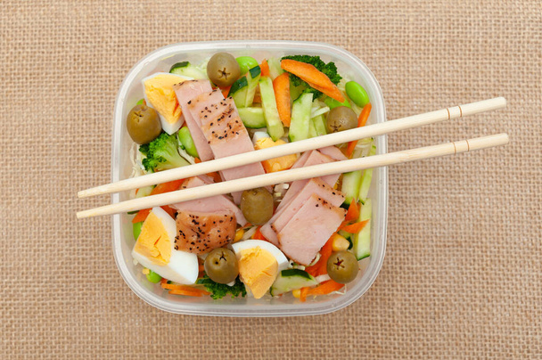 Υγιεινή σαλάτα κοτόπουλο με λαχανικά σε πλαστικό δοχείο με chopstick. Απομονωμένο σε φόντο γιούτας. Στο πάνω μέρος. Οριζόντια βολή. - Φωτογραφία, εικόνα