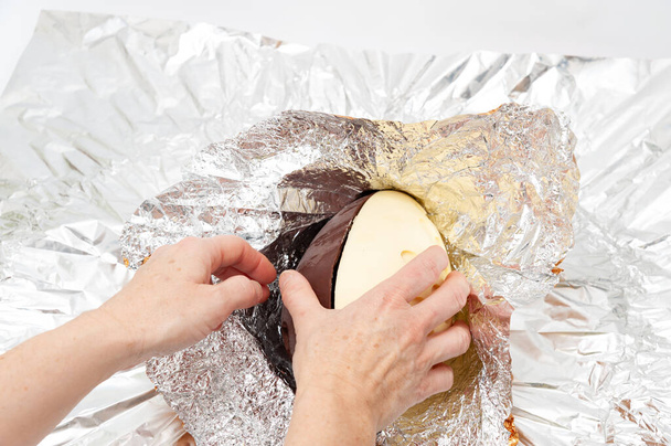 Uovo di Pasqua - Mani disimballaggio fatto in casa uovo di cioccolato avvolto in foglio di alluminio. Copia spazio. - Foto, immagini