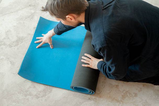 een man rolt de yoga mat op de vloer in yoga klasse workout - Foto, afbeelding