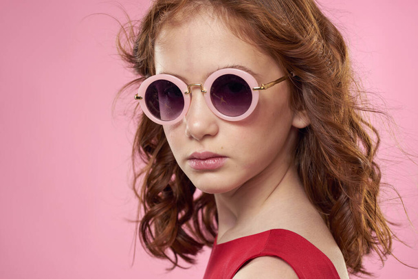 Girl with curly hair dark round glasses fun red dress pink background - Valokuva, kuva