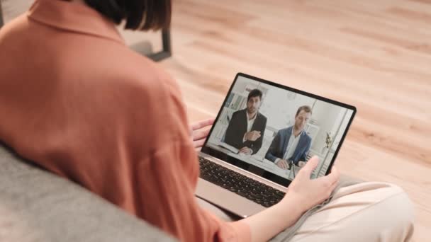 Angle élevé au-dessus de l'épaule d'une personne méconnaissable assise sur le sol avec un ordinateur portable sur ses genoux, ayant une vidéoconférence avec deux hommes d'affaires professionnels divers parlant - Séquence, vidéo