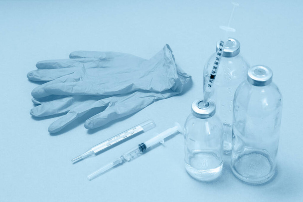 Sıvı ilaç için cam şişeler, iğne için şırıngalar, termometre ve lateks eldivenler. Mavi renkte bir resim. Üst Manzara. Sağlık ve Tıp Konsepti. - Fotoğraf, Görsel
