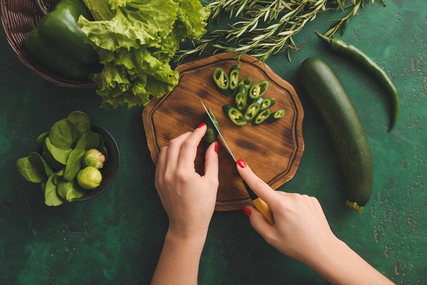 Vrouw snijden groene chili pepers op kleur achtergrond - Foto, afbeelding