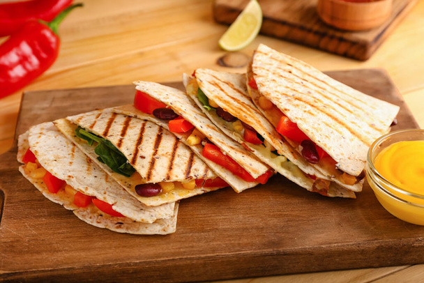 Board with tasty vegetarian quesadillas and sauce on wooden background - Photo, Image
