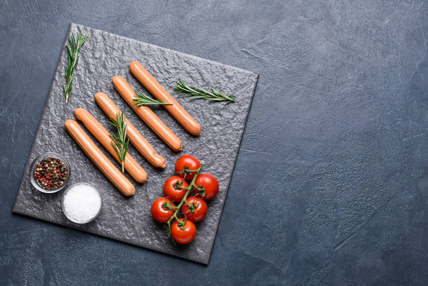 Slate plate with tasty sausages, spices and tomatoes on dark background - Photo, Image