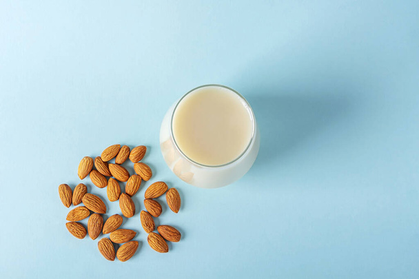 Glass of organic vegan dairy free milk from almonds nuts. Healthy breakfast with vegetarian alternative drink on blue background. Copy space for text - 写真・画像