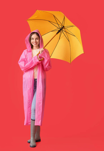 Stylish young woman in raincoat and with umbrella on color background - Photo, Image