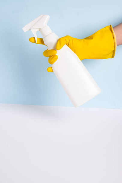 Woman hand in yellow rubber protective glove holding white plastic spray bottle one blue background. General or regular cleanup. Empty place for text or logo. . High quality photo - Fotoğraf, Görsel