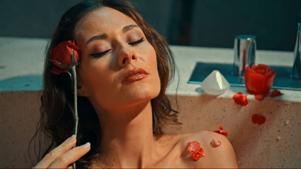 Young European girl long-haired brunette lies in the bathroom with red flowers on spa procedure - Fotó, kép