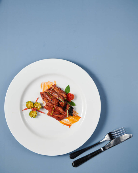A vertical top view of decorated cooked meat with sauce served on a white plate - Foto, immagini