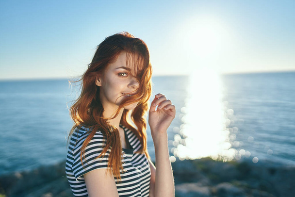 red-haired woman in a t-shirt near the sea at sunset in the mountains in nature. High quality photo - 写真・画像