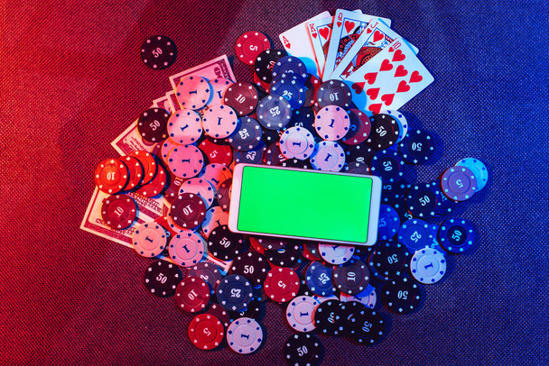 Het concept van een online casino: speelkaarten, wedchips en een smartphone met een kopieerruimte en een groene achtergrond. Bovenaanzicht. - Foto, afbeelding