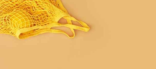 Mesh shopping bag with lemon on beige canvas background. Banner for design - Photo, Image