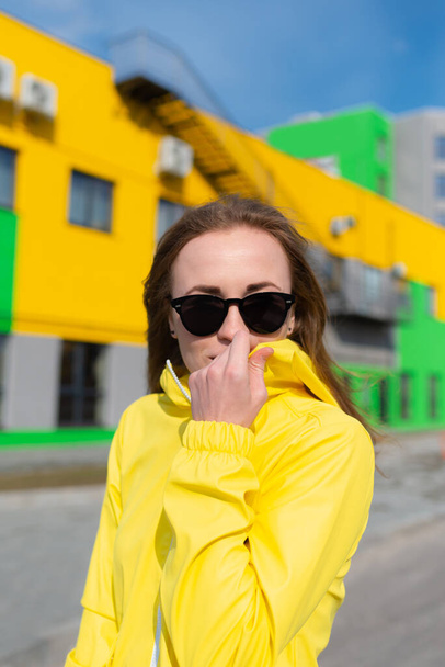 Soğuk bahar havasını kucaklayan genç bir kadın sıcacık sarı ceketini giyip sokakta geziniyor. - Fotoğraf, Görsel
