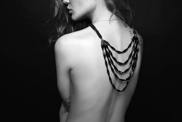 mooie jonge vrouw met ketting op haar naakte rug. sexy meisje met sieraden - Foto, afbeelding