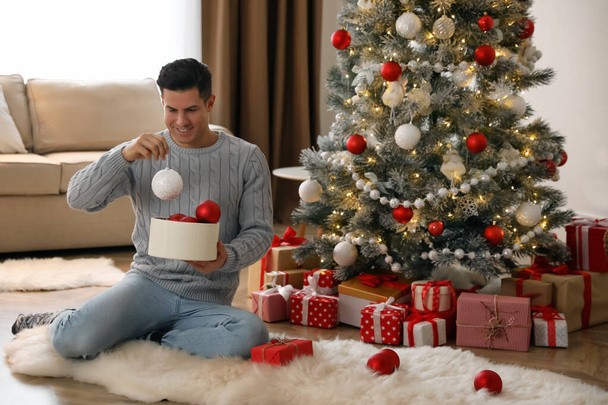 Handsome man decorating Christmas tree at home - Foto, imagen