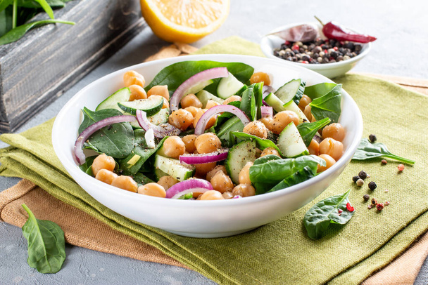 Chickpea salad with cucumber, spinach, parsley, onions and lemon in a plate on a served table, selective focus. Tasty and healthy vegetarian food, oriental and Mediterranean cuisine. - Фото, изображение