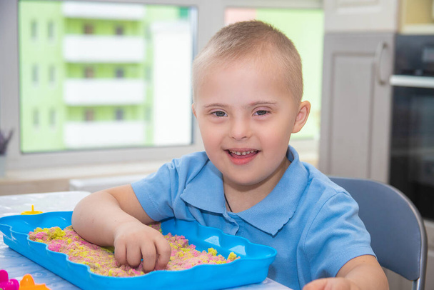 Retrato de un niño lindo con síndrome de Down, un niño que juega con arena y moldes para modelar, desarrollo temprano, niños andwalids. - Foto, Imagen