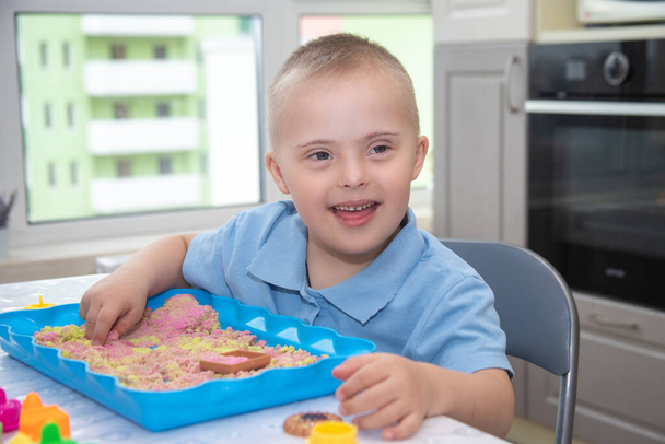 Retrato de um menino bonito com síndrome de Down, uma criança brincando com areia e moldes para modelagem, desenvolvimento precoce, crianças e walids. - Foto, Imagem