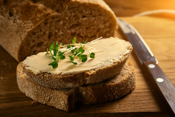 Kézműves szeletelt pirítós kenyér vajjal és mikrozöld brokkolival fából készült vágódeszkán késsel. Egyszerű reggeli.. - Fotó, kép